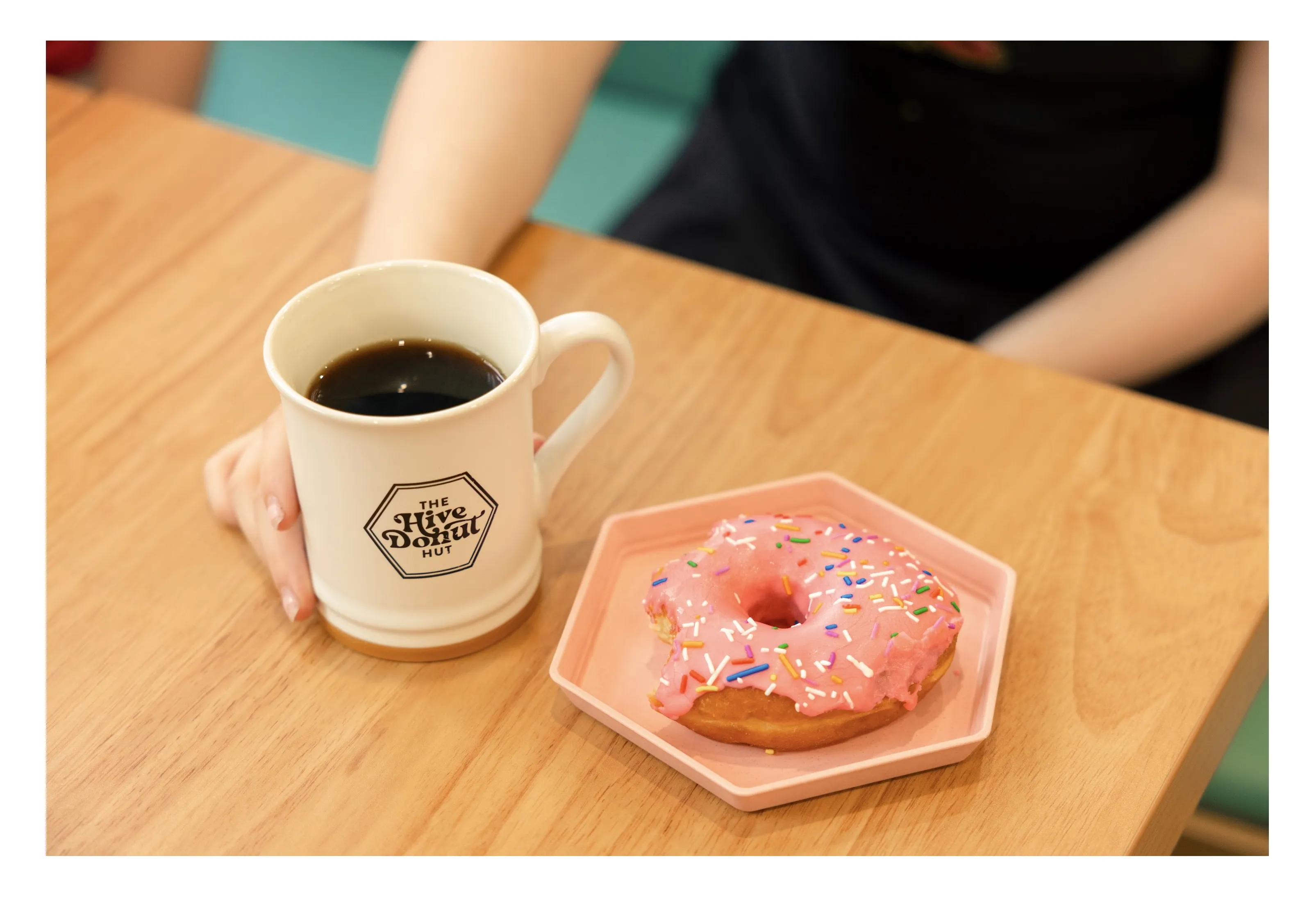A glazed donut served beside a fresh cup of coffee on a table at The Hive Donut Hut.